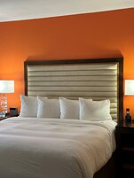 Una camera d'albergo con un letto grande, biancheria da letto bianca e una parete arancione.