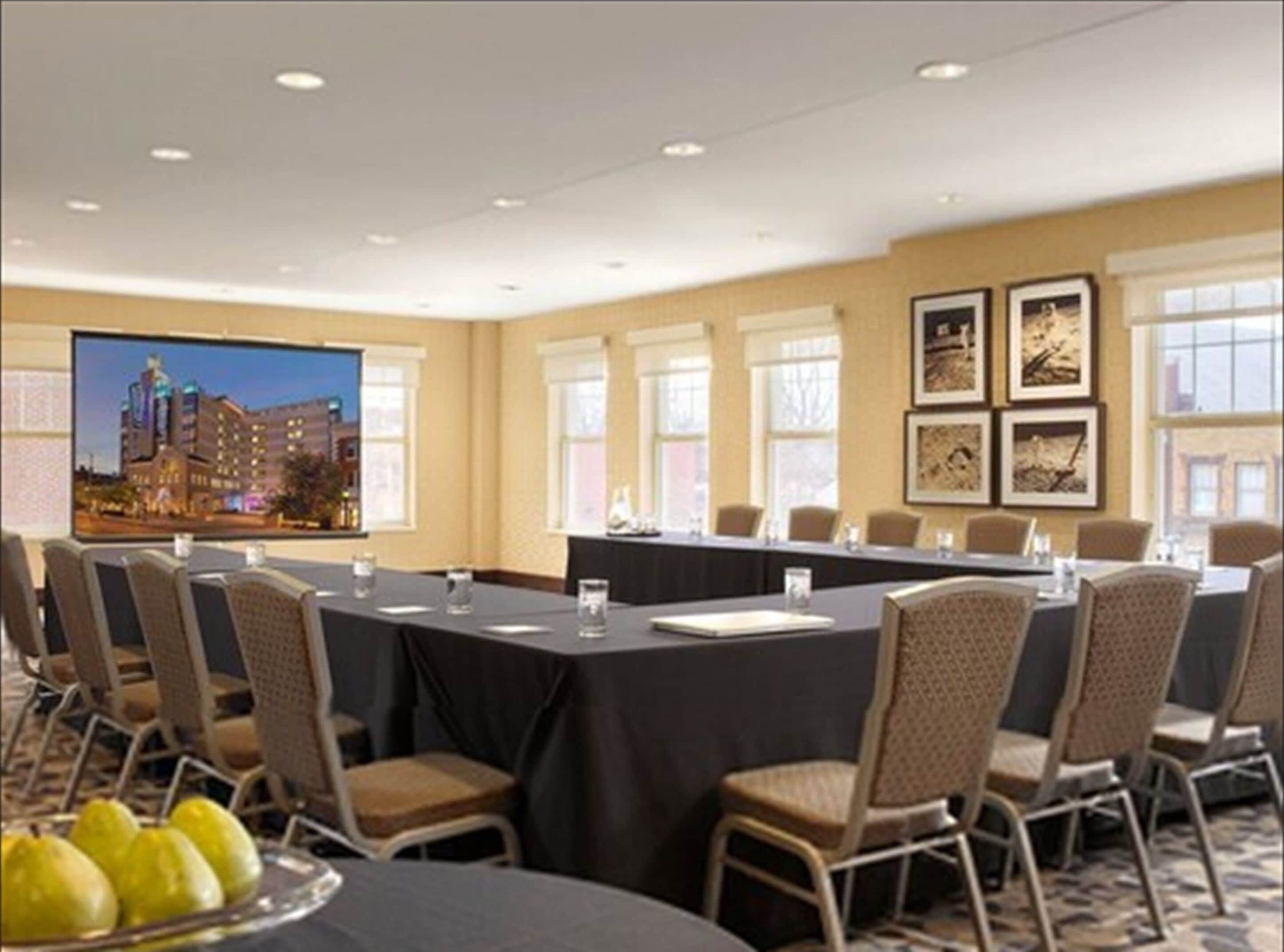 A conference room with a long table, chairs, a projector screen, and framed pictures on the wall.