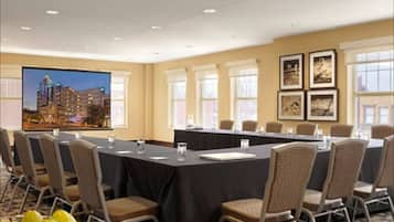 A conference room with a long table, chairs, a projector screen, and framed pictures on the wall.
