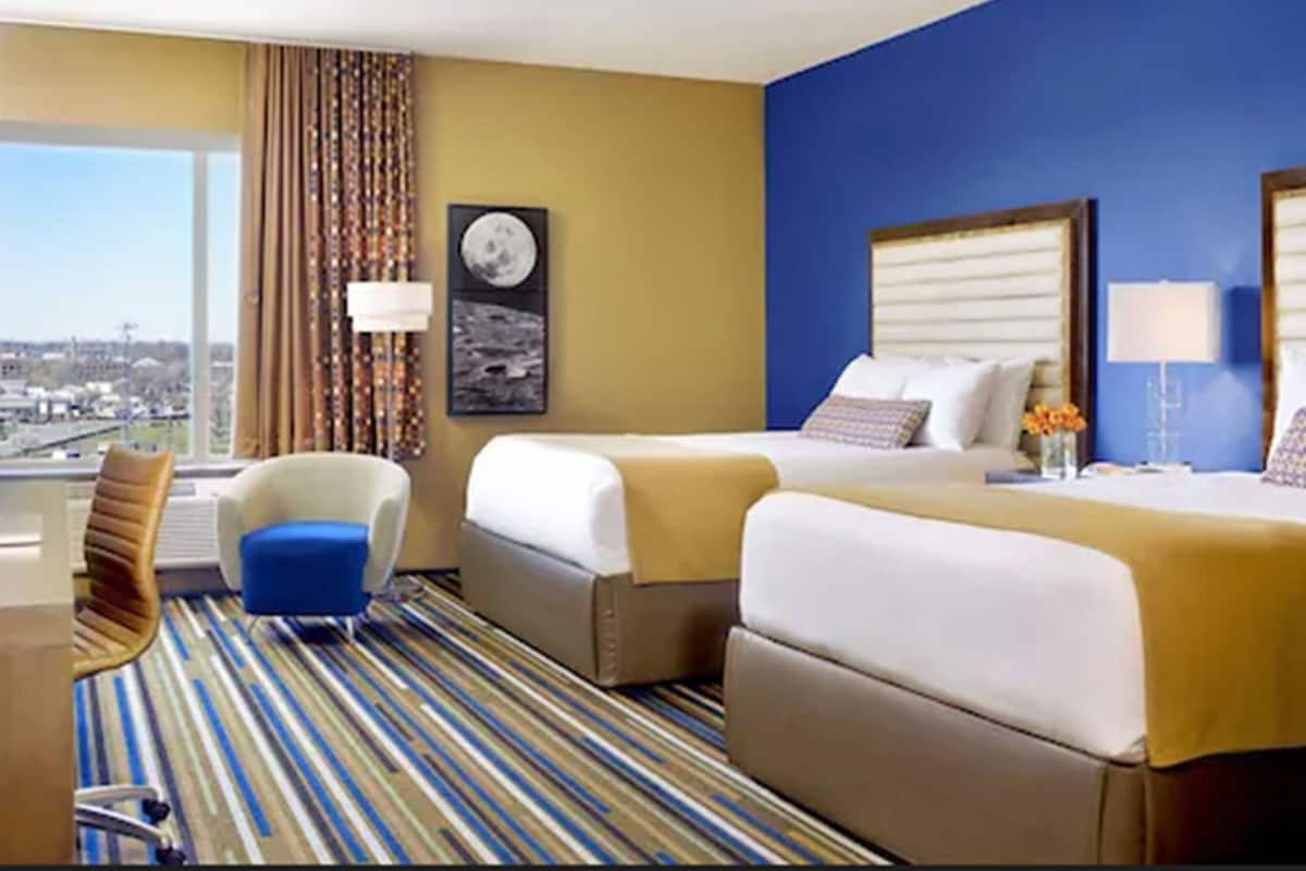 A hotel room with a large window, a bed, a chair, and a desk.