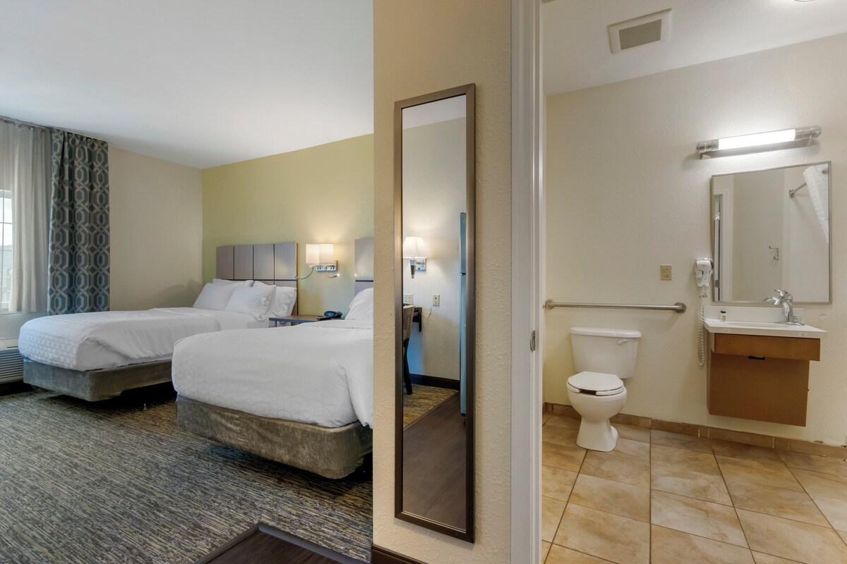 A hotel room with two beds, a bathroom with a toilet, sink, and mirror.