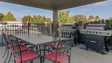 Un patio al aire libre con mesa y sillas, una parrilla y vistas al estacionamiento y árboles.