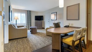 Ein Hotelzimmer mit Essbereich, einer Couch, einem Fernseher und einer Lampe.