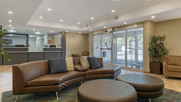Eine moderne Lobby mit einem braunen Ecksofa, einem runden Hocker und einem großen Fenster mit Blick auf die Straße.