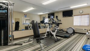Ein Fitnessraum mit Trainingsgeräten, einem Spiegel, einer Uhr und einem Fernseher an der Wand.