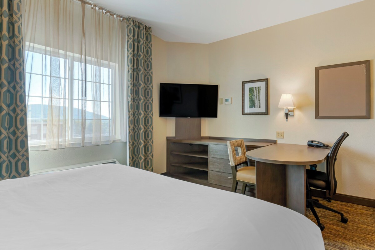 A hotel room with a large bed, a desk with a chair, a flat-screen TV, a lamp, and a framed picture on the wall.