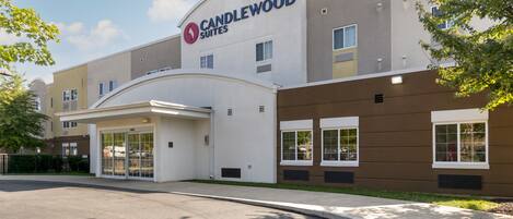 A modern hotel with a prominent "CANDLEWOOD SUITES" sign, a covered entrance, and a parking area.