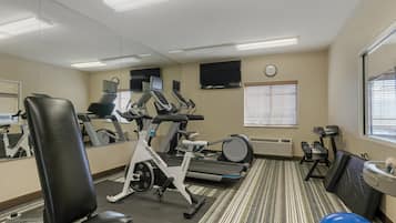 A gym with exercise equipment, a mirrored wall, a clock, and a window with blinds.