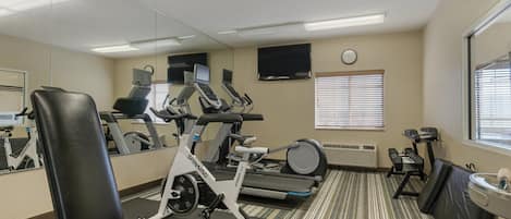 A gym with exercise equipment, a mirrored wall, a clock, and a window with blinds.