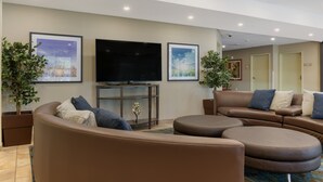 Ein modernes Wohnzimmer mit großem Flachbildfernseher, bequemen Sitzmöglichkeiten und gerahmten Kunstwerken an den Wänden.