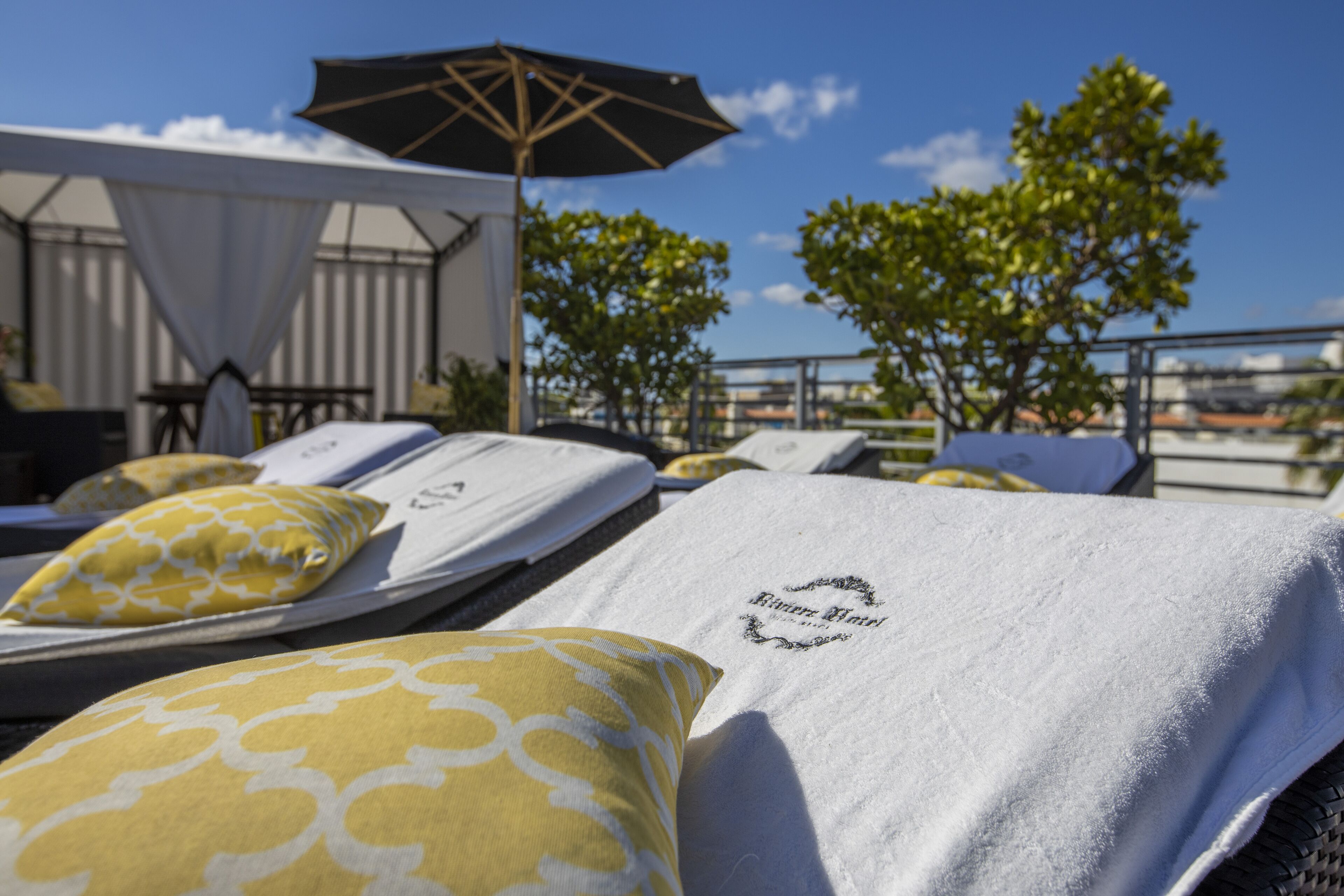 A rooftop lounge area with sunbeds, towels, and an umbrella.