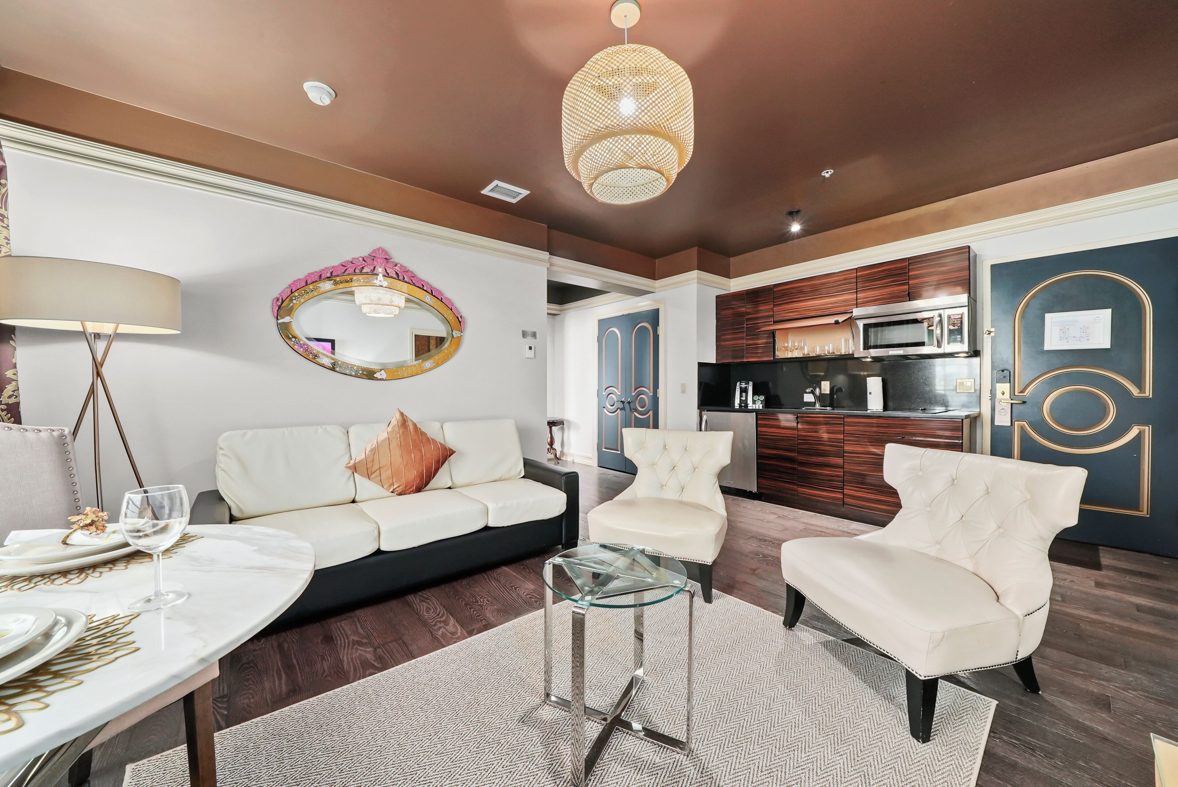 A modern living room with a white sofa, two armchairs, a glass coffee table, and a dining area with a table set for two.