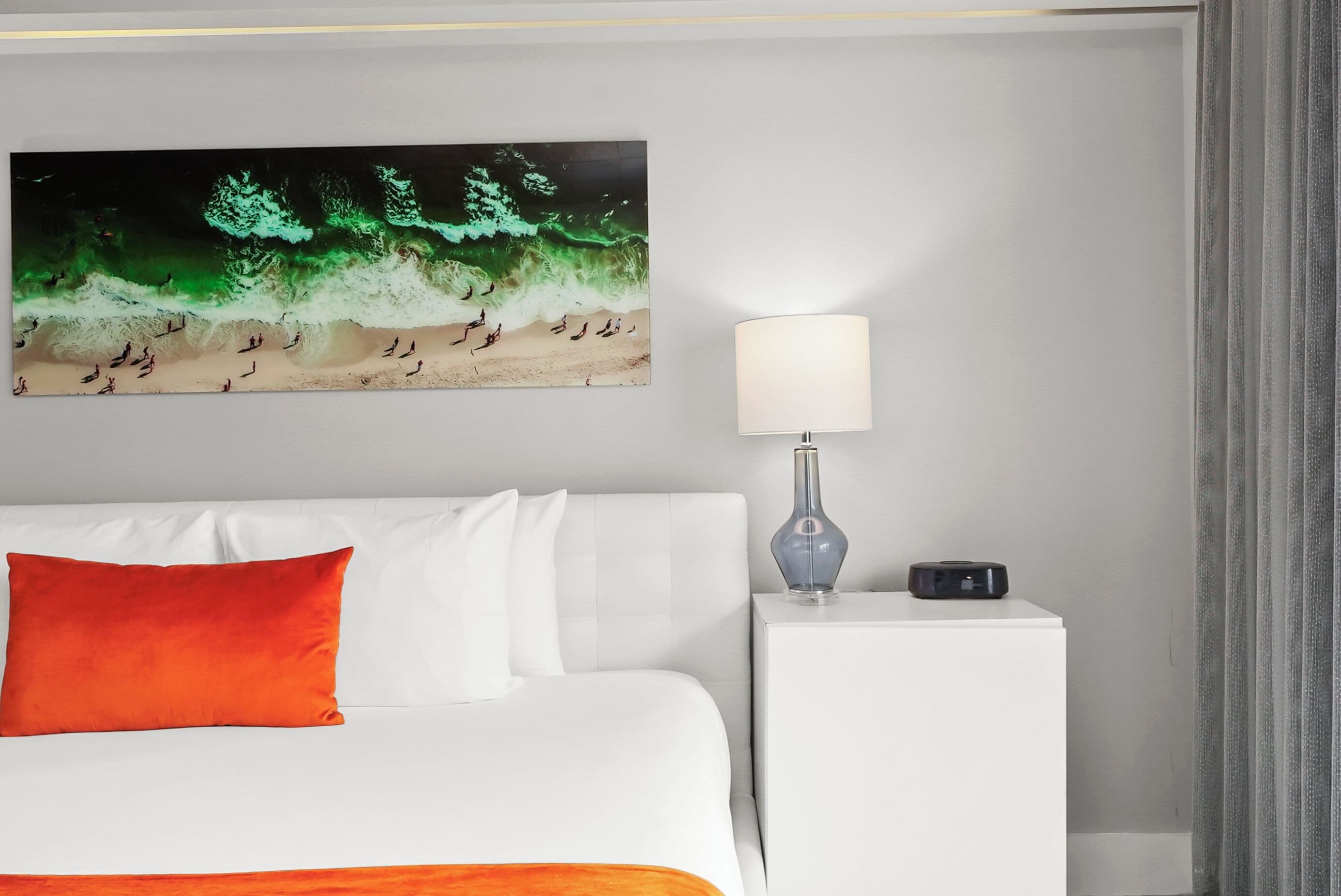 A hotel room with a bed, a nightstand with a lamp, and a wall-mounted artwork.