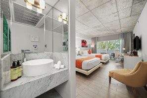 Un bany modern amb un envàs gran i un mirall, una zona de dutxa i articles de tocador. L'habitació té un llit amb roba de llit taronja, un escriptori i una cadira.