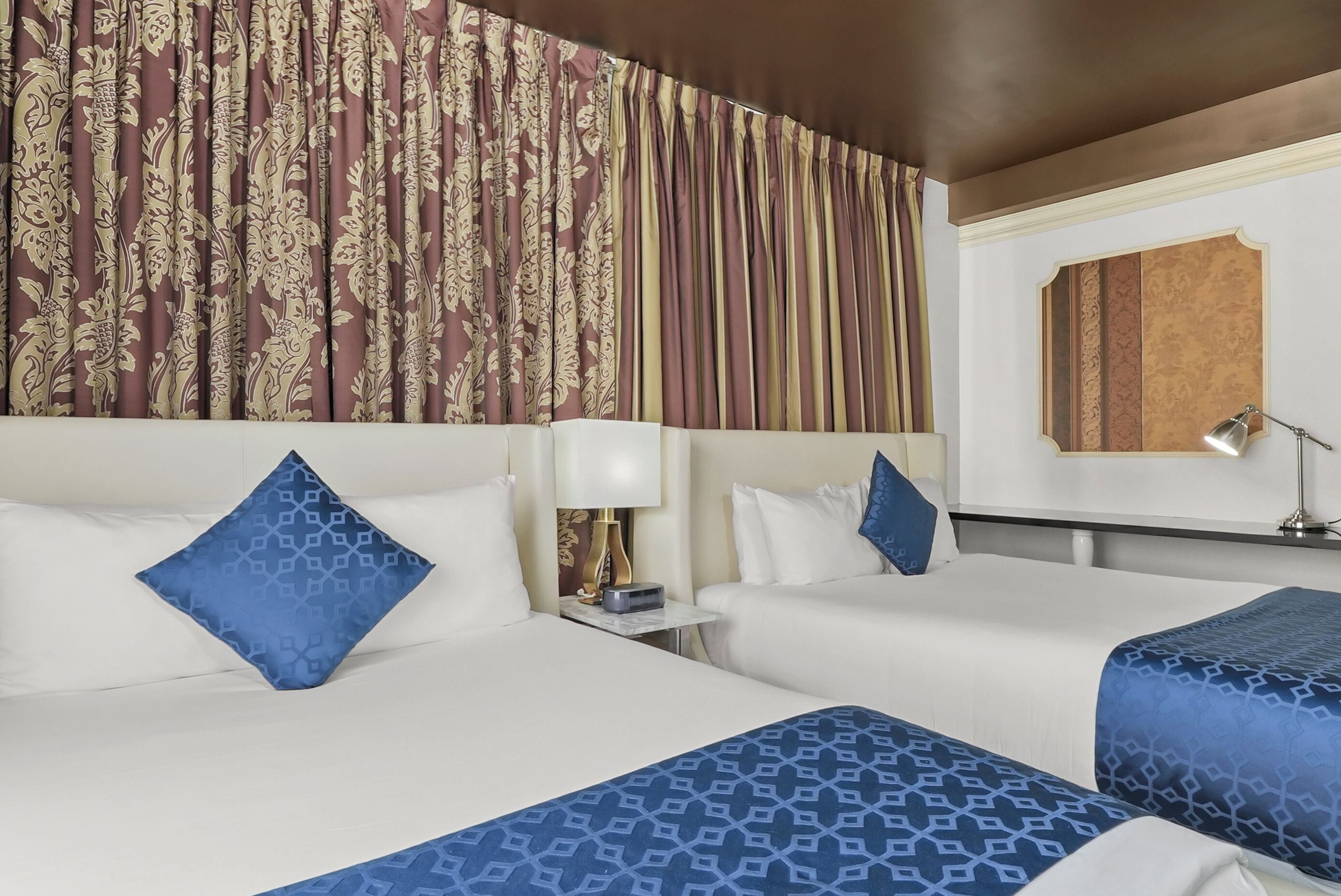 A hotel room with two beds, a nightstand with a lamp, and a large patterned curtain.