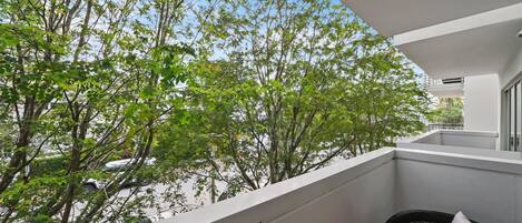 A balcony with a wicker chair and a red cushion, overlooking a tree-lined street.