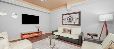 A modern living room with a flat-screen TV, a glass coffee table, a sofa, a side table, and a floor lamp.