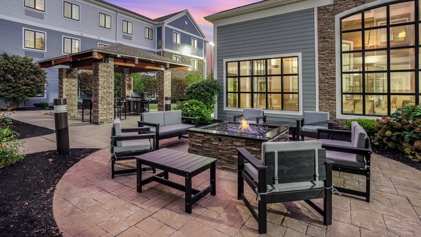 A patio area with outdoor furniture, a fire pit, and a stone fireplace. - Staybridge Suites Williamsville Buffalo by IHG (Buffalo)