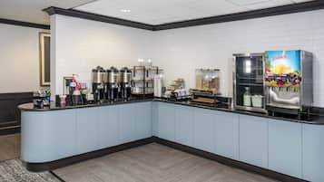 Una estación de bebidas de autoservicio con cafeteras, dispensadores de té y un dispensador de jugo.