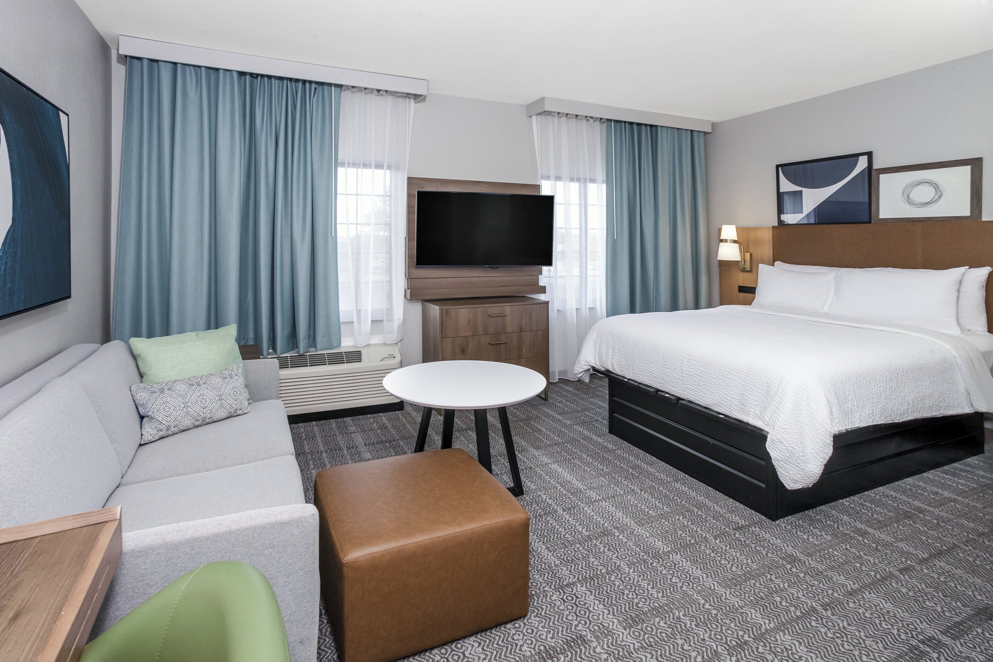 Quarto de hotel com cama, sofá, televisão, mesa pequena e uma cadeira.