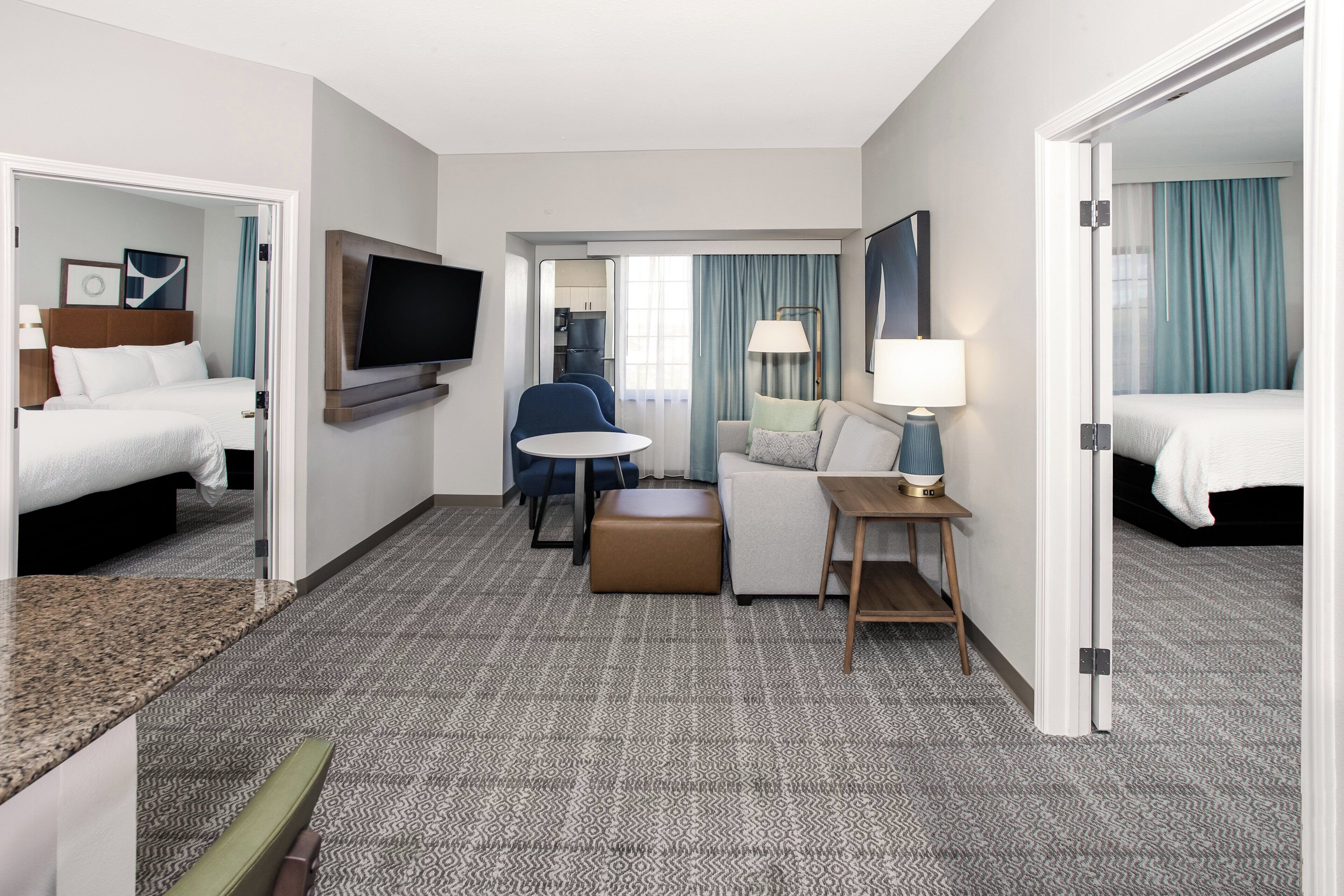 Habitación de hotel con cama, televisor, escritorio con silla, sofá, lámpara y una mesita.