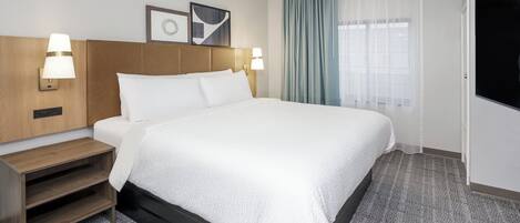 A hotel room with a large bed, two bedside lamps, a wooden nightstand, a TV, and a window with curtains.