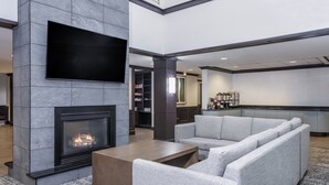 A modern living room with a fireplace, grey sofas, and a flat-screen TV mounted on the wall. - Staybridge Suites Williamsville Buffalo by IHG (Buffalo)