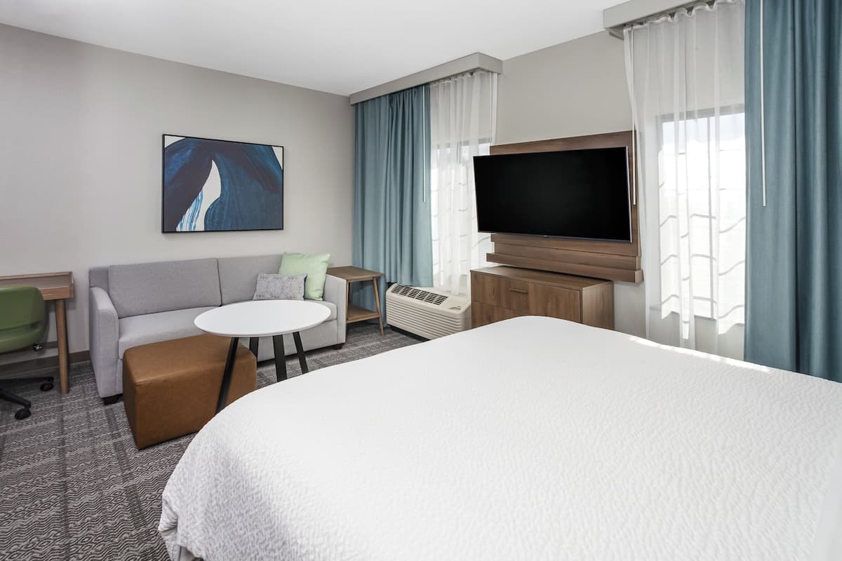 Hotellihuone, jossa on suuri sänky, sohva, pieni pöytä, televisio ja taulu seinällä.