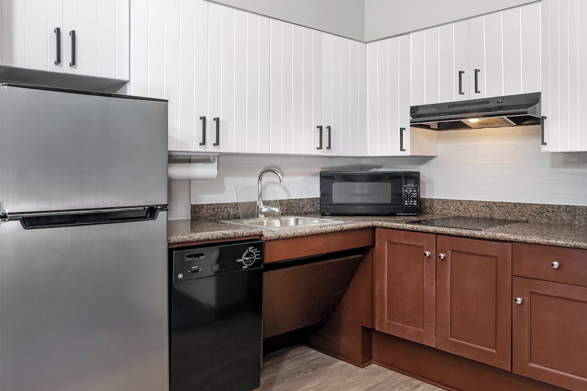 Una cocina moderna con armarios blancos, un refrigerador de acero inoxidable, un lavavajillas, un microondas y una encimera de granito.