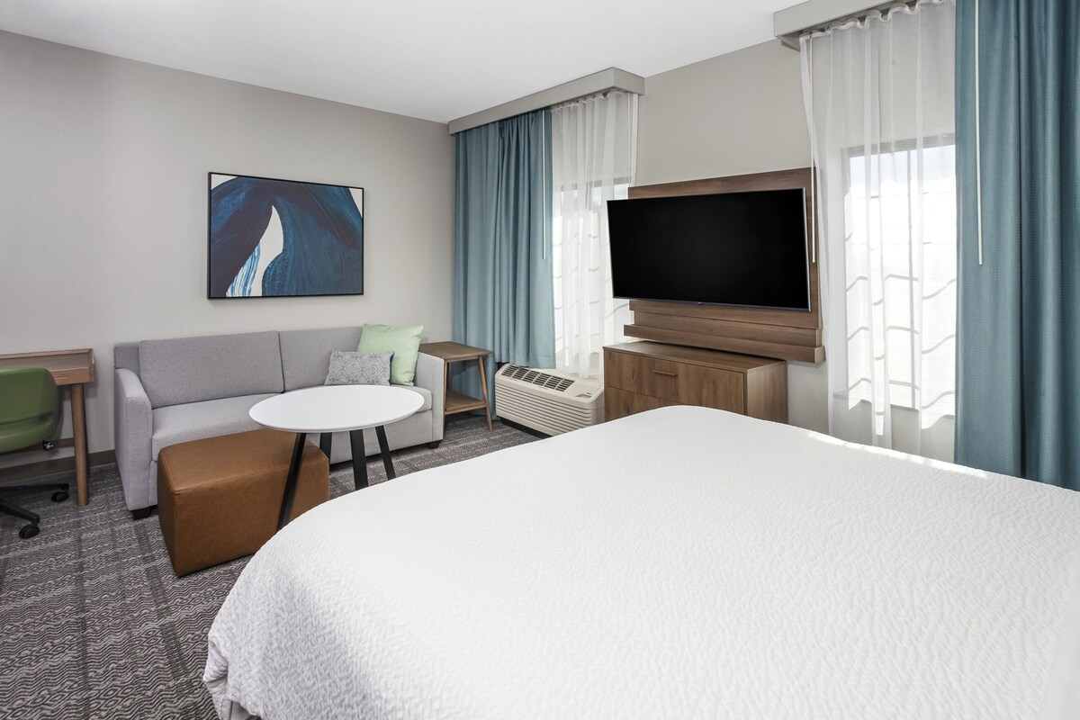 Una habitación de hotel con una cama grande, un sofá, una mesita, un televisor y un cuadro en la pared.