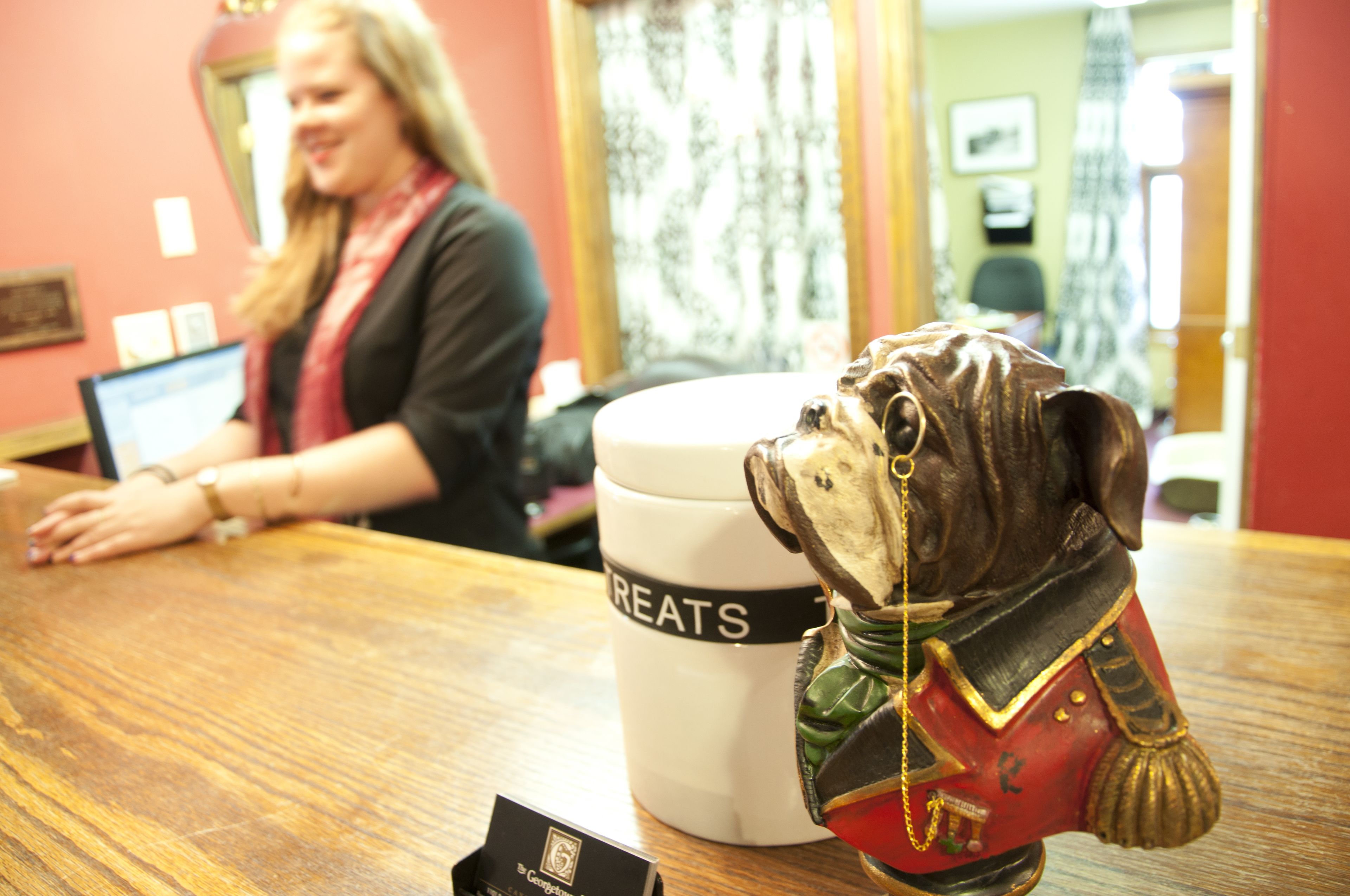 A receptionist behind a counter with a decorative dog figurine and a 'Treats' mug.