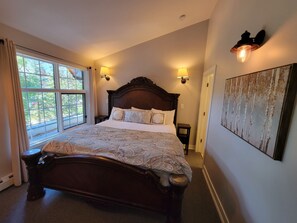 A large bed with a wooden headboard, two bedside tables, and a window with curtains.