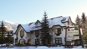 A Georgian-style building with a snow-covered roof, large windows, and a sign for The Georgetown Inn Restaurant & Pub. - The Georgetown Inn (Canmore)