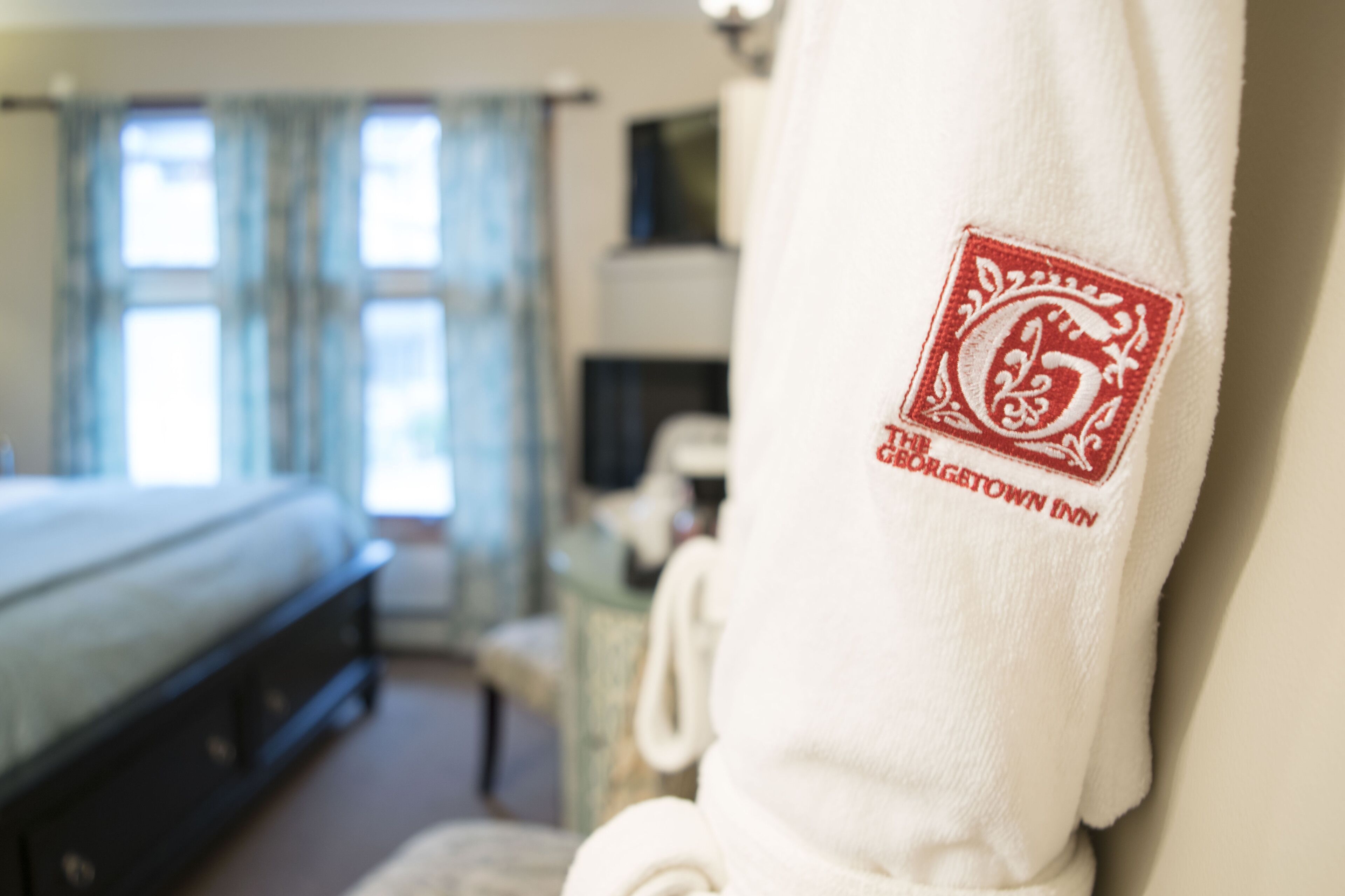 A hotel room with a bed, a chair, and a robe with a logo.