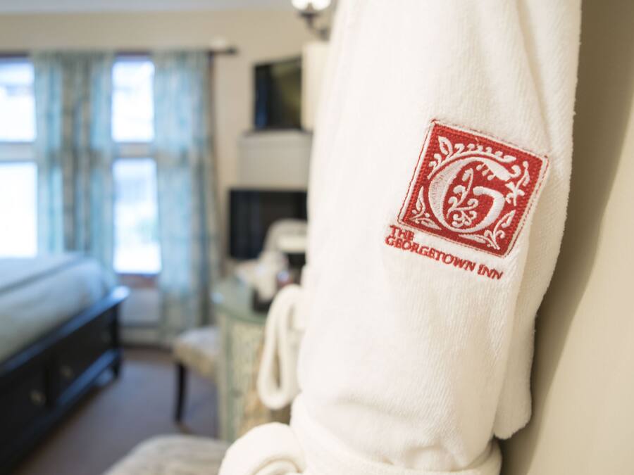 A hotel room with a bed, a chair, and a robe with a logo.