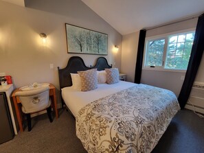 A bedroom with a large bed, a bedside table, a chair, a window with a view of trees, and a wall-mounted artwork.