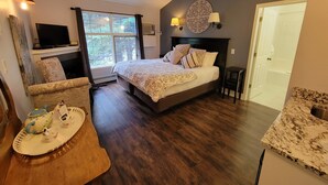 A bedroom with a large bed, a TV, a fireplace, and a view of the outdoors. - The Georgetown Inn (Canmore)