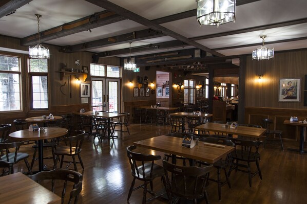 A restaurant with wooden tables and chairs, hanging lights, and framed pictures on the walls.
