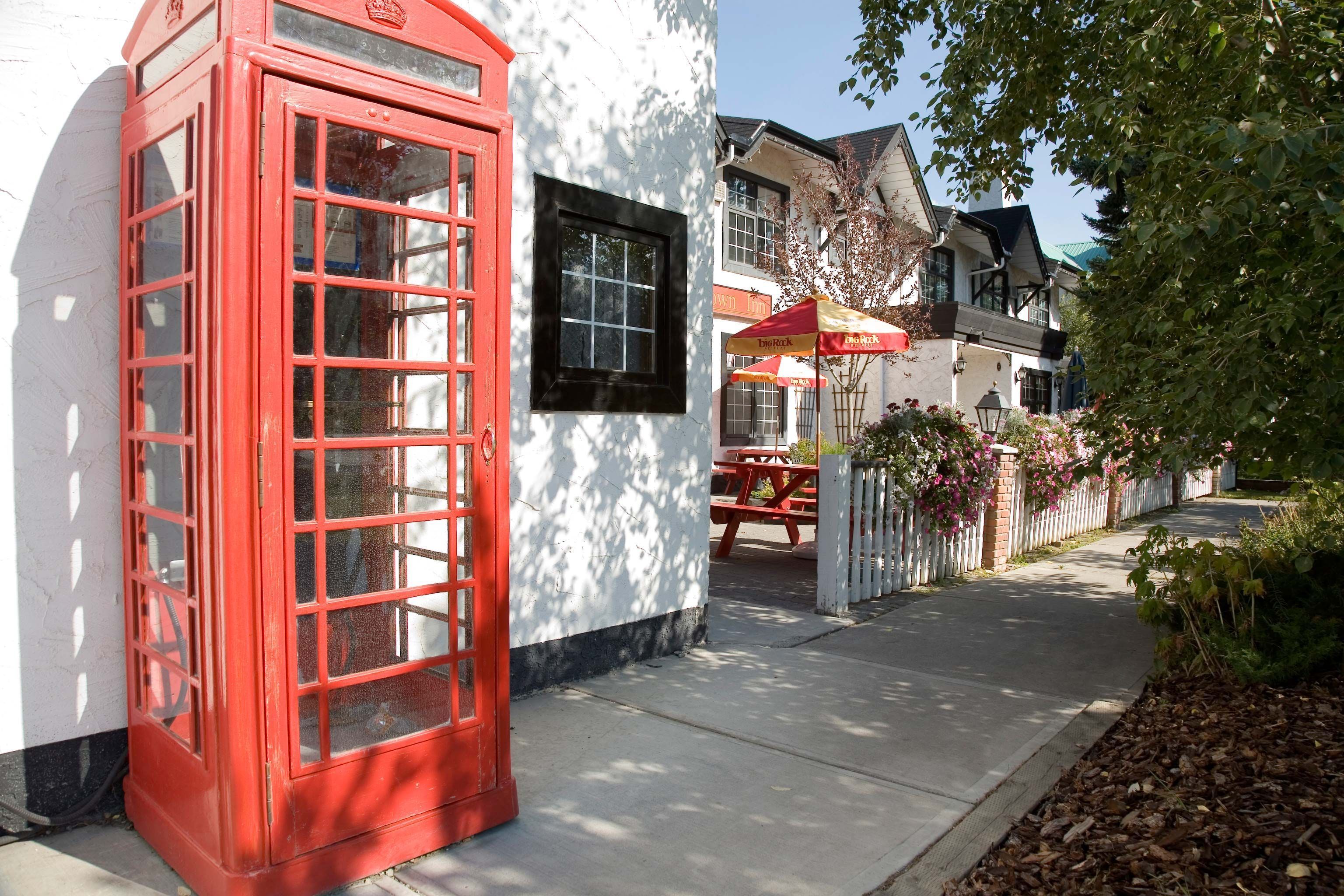 Une cabine téléphonique rouge traditionnelle, un bâtiment blanc avec une fenêtre noire, et un parapluie rouge et jaune.