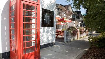 Une cabine téléphonique rouge traditionnelle, un bâtiment blanc avec une fenêtre noire, et un parapluie rouge et jaune.