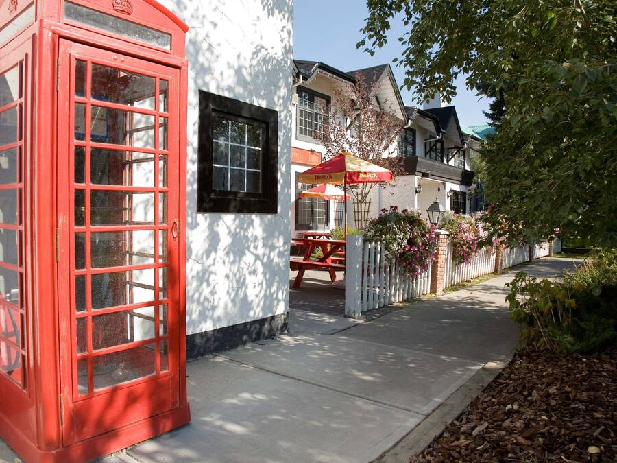 Une cabine téléphonique rouge traditionnelle, un bâtiment blanc avec une fenêtre noire, et un parapluie rouge et jaune.