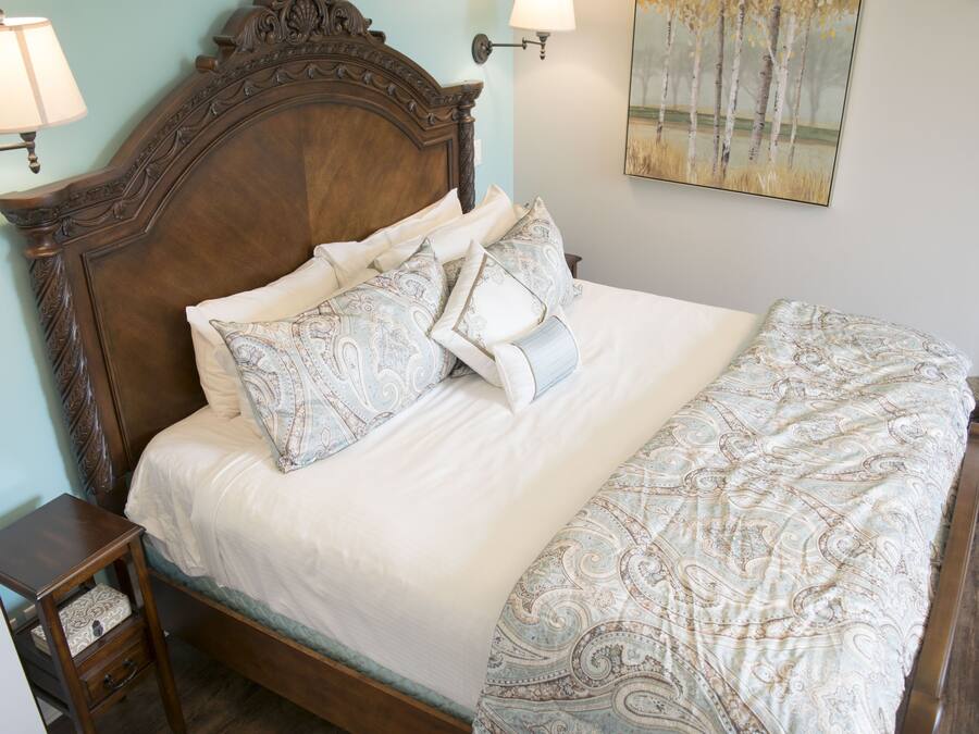 A neatly made bed with patterned bedding, a wooden headboard, bedside lamps, and a painting on the wall.