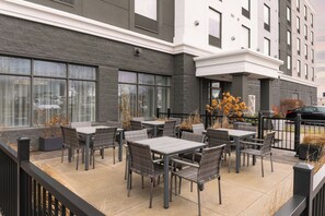 An outdoor patio area with multiple tables and chairs, a black fence, and a building with large windows and a stone facade. - Fairfield by Marriott Inn & Suites Newmarket (Newmarket)