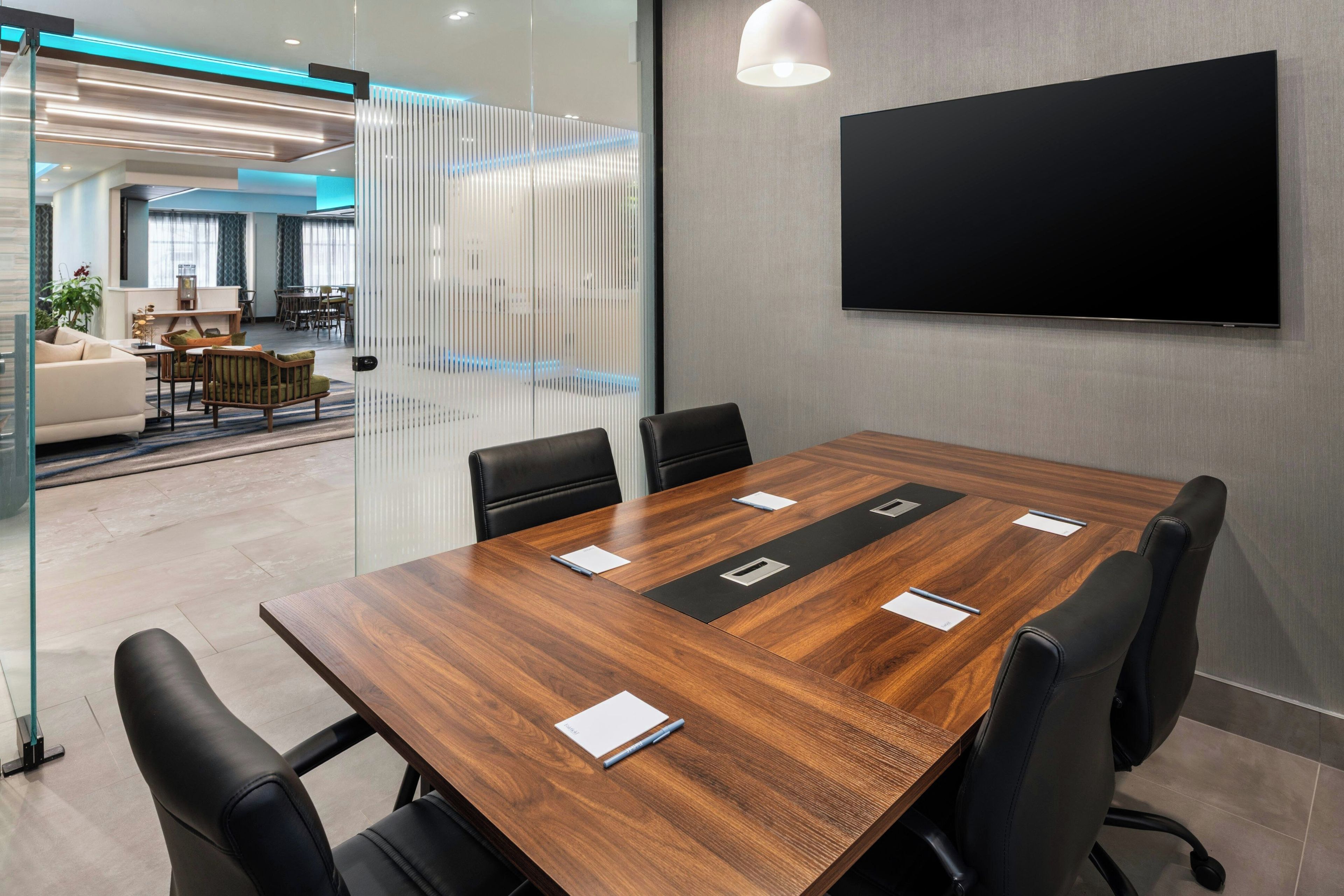 Un salón de conferencias con una mesa de madera, sillas negras y un televisor de pantalla plana en la pared.