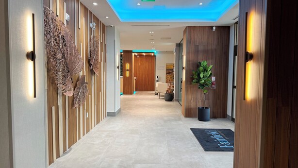 A modern hotel lobby with a wooden reception desk, a large decorative wall, and a potted plant. - Fairfield by Marriott Inn & Suites Newmarket (Newmarket)
