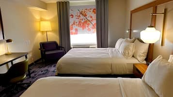 A hotel room with two beds, a desk with a lamp, a chair, and a painting of autumn leaves on the wall.