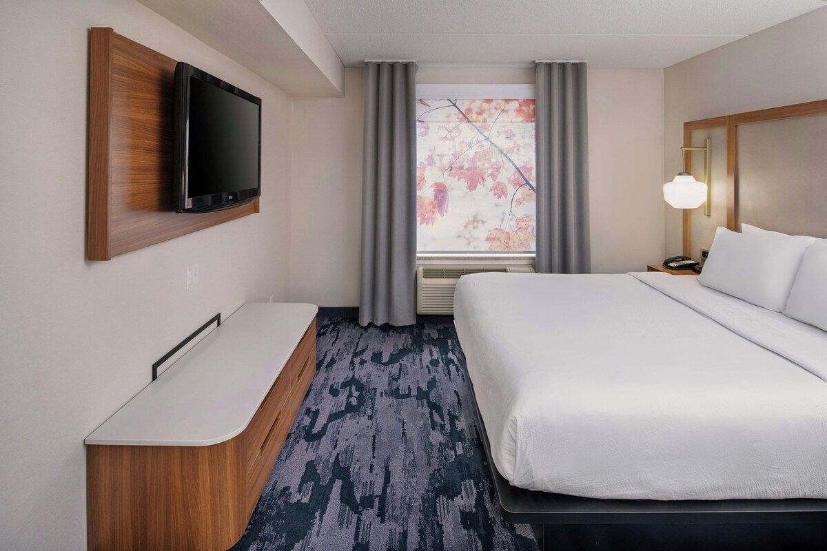 Une chambre d’hôtel avec un lit, un bureau, une télévision, une fenêtre avec des rideaux et une lampe.
