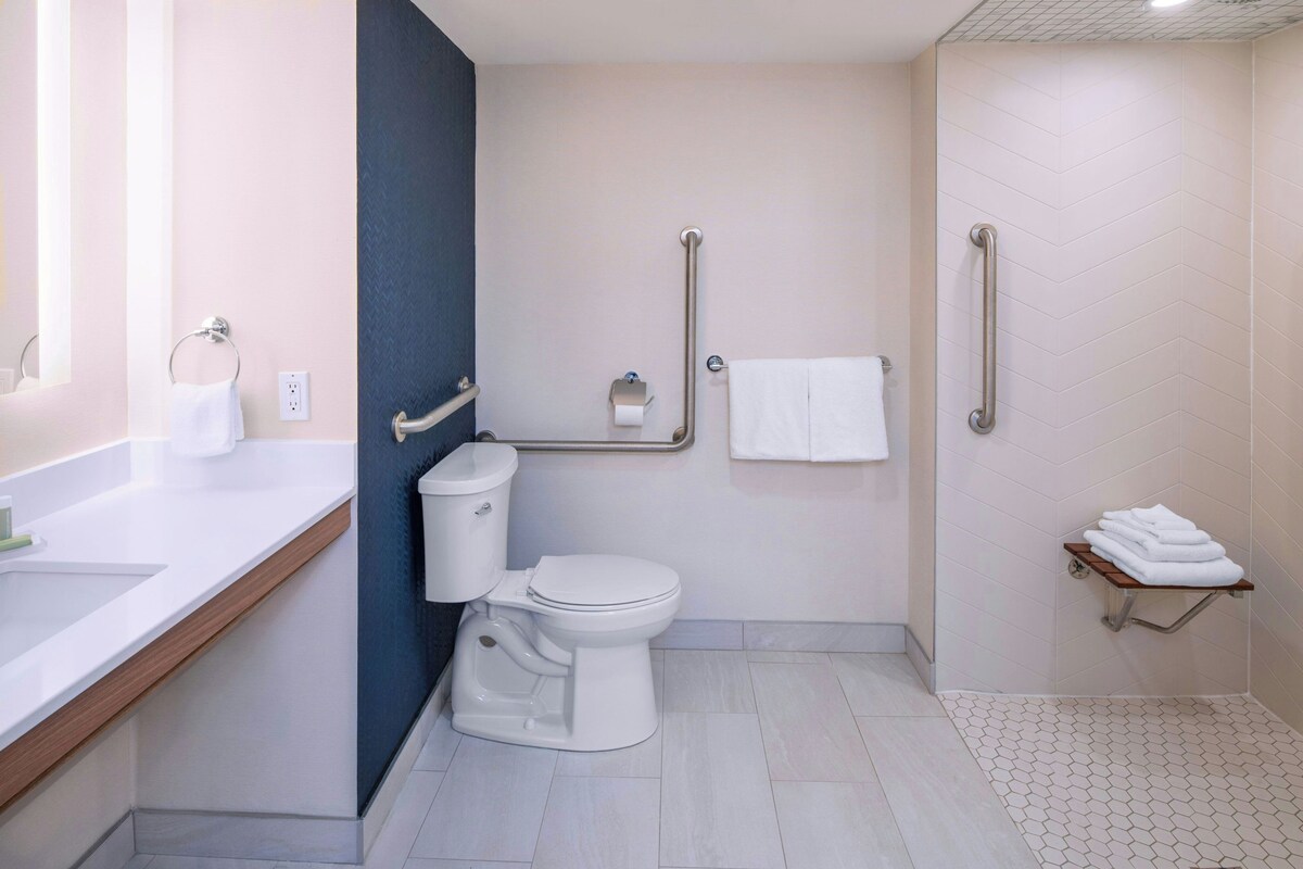 Une salle de bain moderne équipée de toilettes, d’un bidet, de barres d’appui, d’un porte-serviettes et d’une petite étagère avec des serviettes.