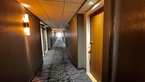 Guest rooms line the carpeted corridor, each with a standard door.