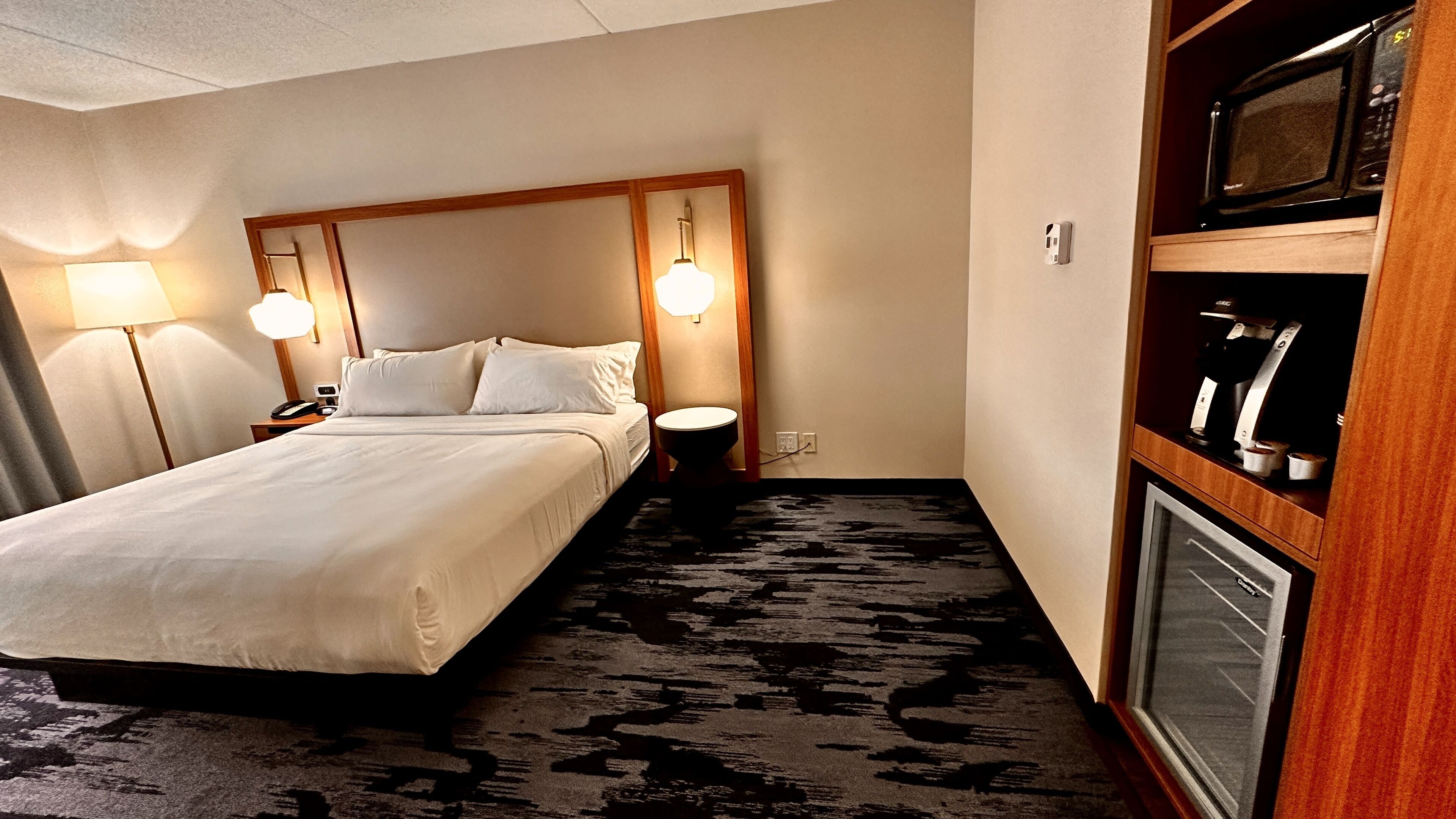 Ett hotellrum med en stor säng, sänglampor, ett litet runt bord, en mikrovågsugn och en kaffemaskin.